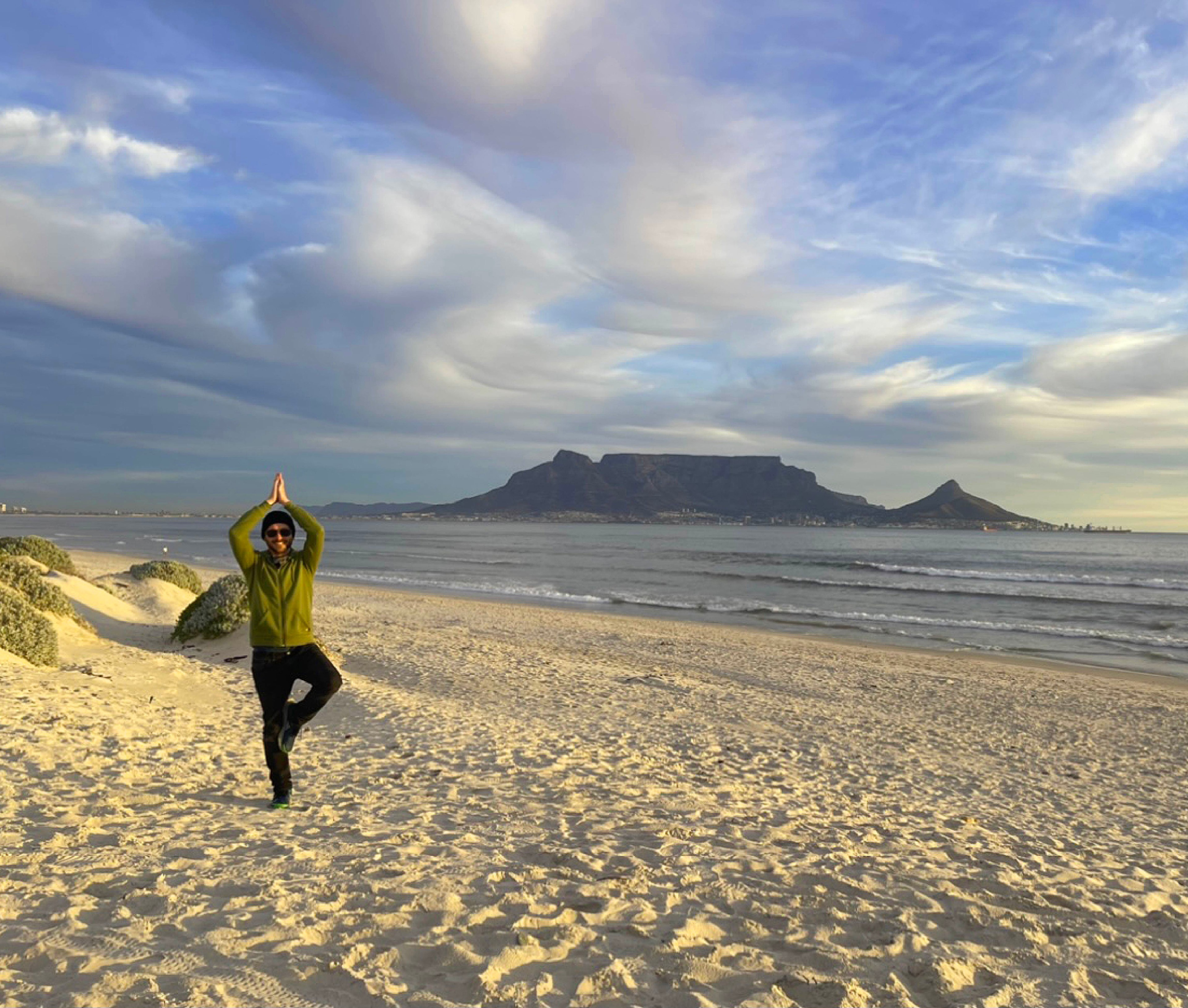 Machiel Bornman doing tree pose on a beach with Table Mountain in the background